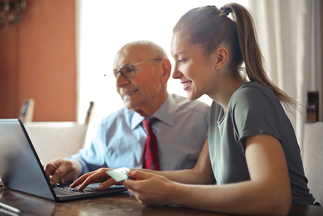 Une personne âgée et une assistante assis devant un ordinateur portable